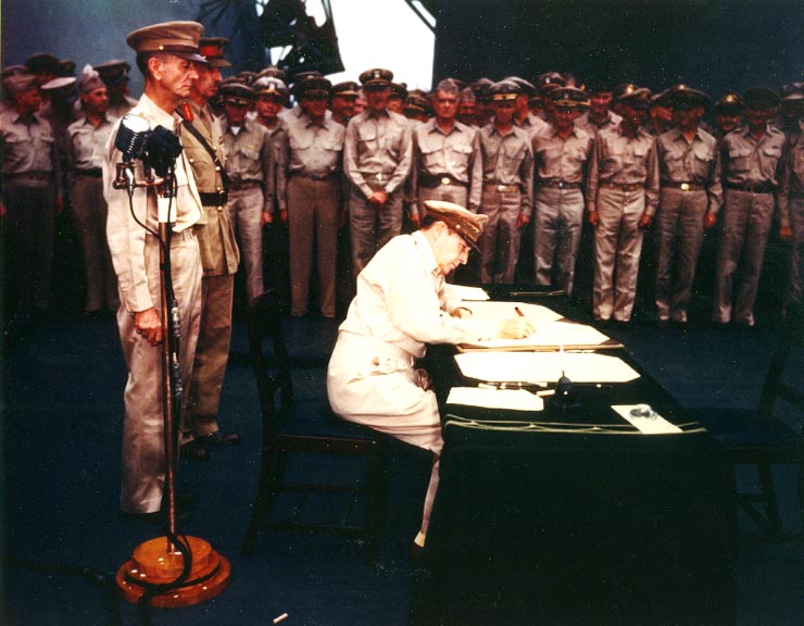 MacArthur signs Japanese surrender instrument aboard USS Missouri. Generals Wainwright and Percival stand behind him.|alt=MacArthur is seated a small desk, writing. Two men in uniform stand behind him. A large crowd of men in uniform look on.