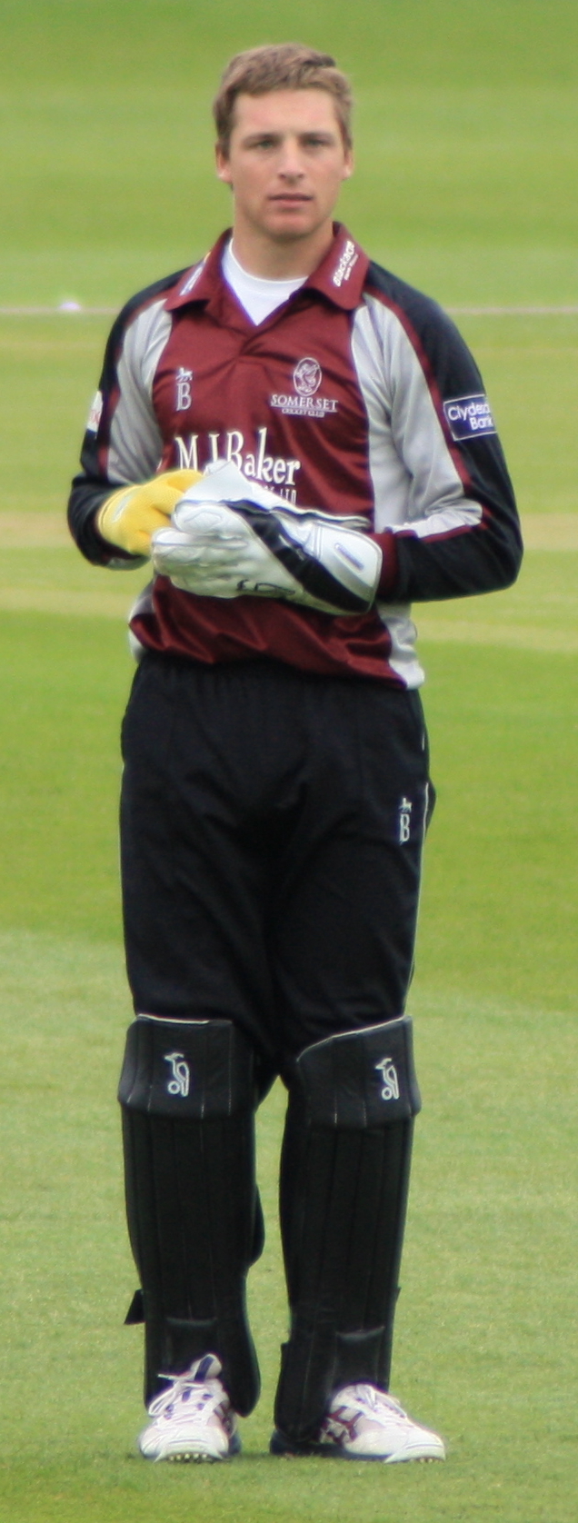Jos Buttler current English keeper|alt=A young man with light brown hair is standing on some grass. He is wearing a burgundy, grey and black cricket uniform, large gloves and black trousers covered by black think pads on his lower legs. Jos Buttler current English keeper|alt=A young man with light brown hair is standing on some grass. He is wearing a burgundy, grey and black cricket uniform, large gloves and black trousers covered by black think pads on his lower legs.
